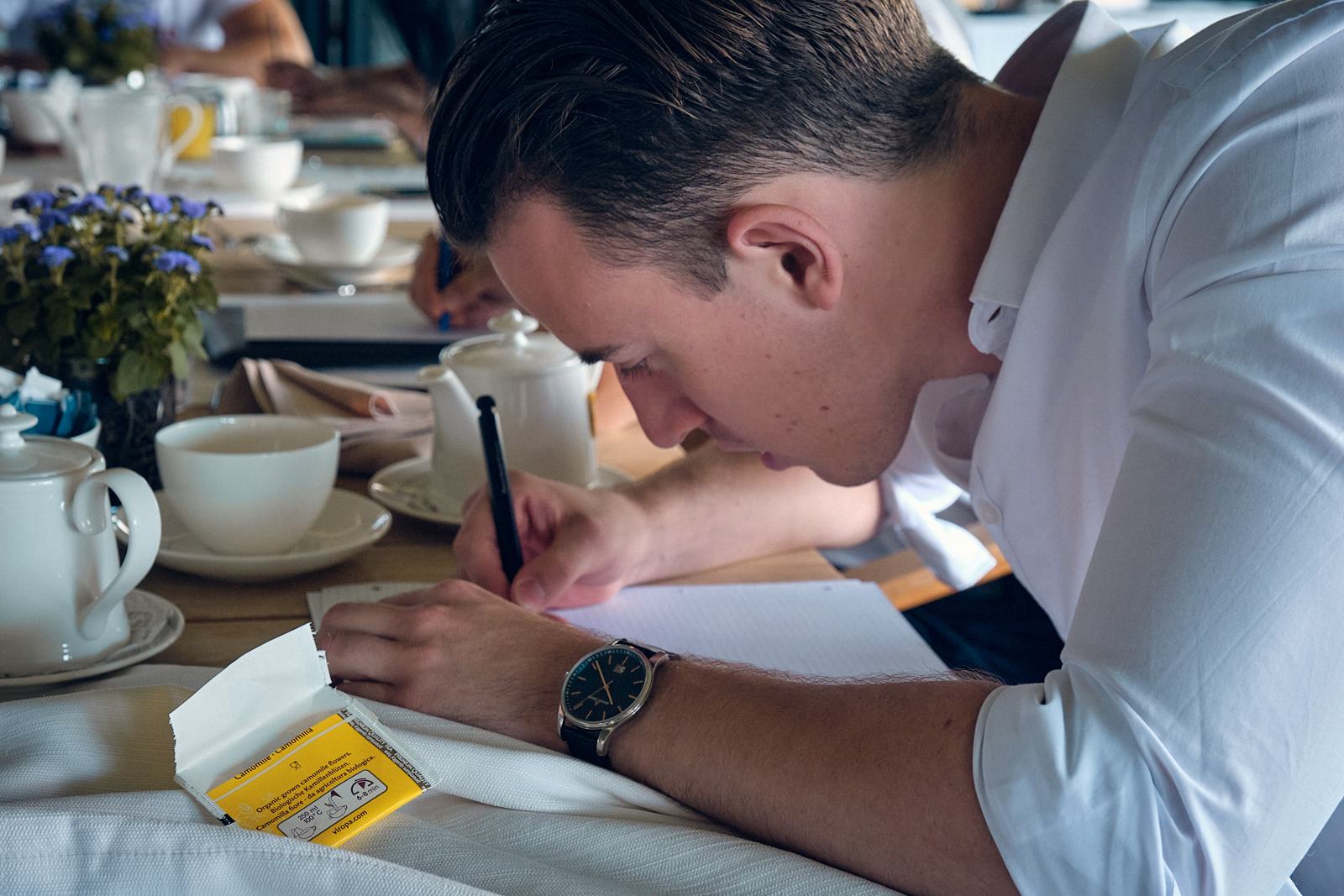 Ein Teilnehmer schreibt konzentriert in ein Notizbuch, daneben eine Kaffeetasse.