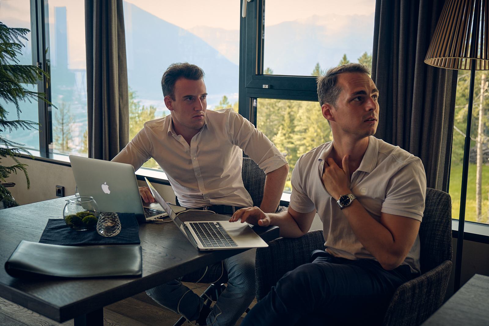 Zwei Teilnehmer arbeiten gemeinsam an einem Laptop vor einem Fenster mit Bergblick.
