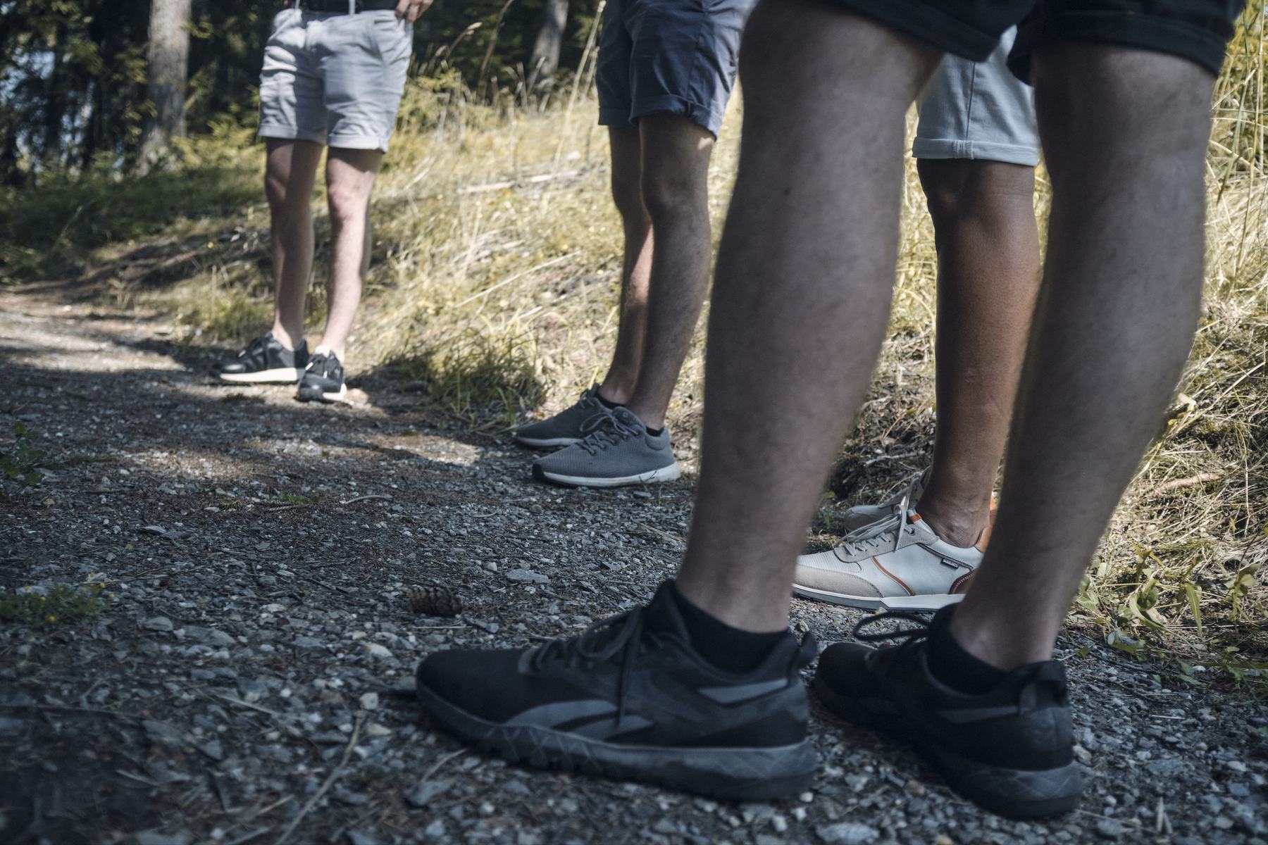 Beine mehrerer Wanderer auf einem Schotterweg im Gebirge.